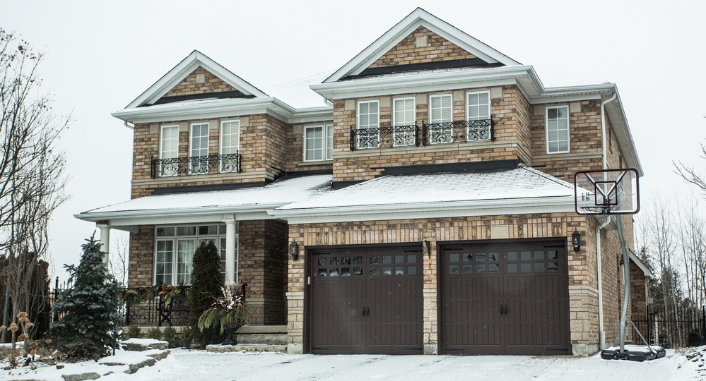 A big house with snow on the roof and the front yard.